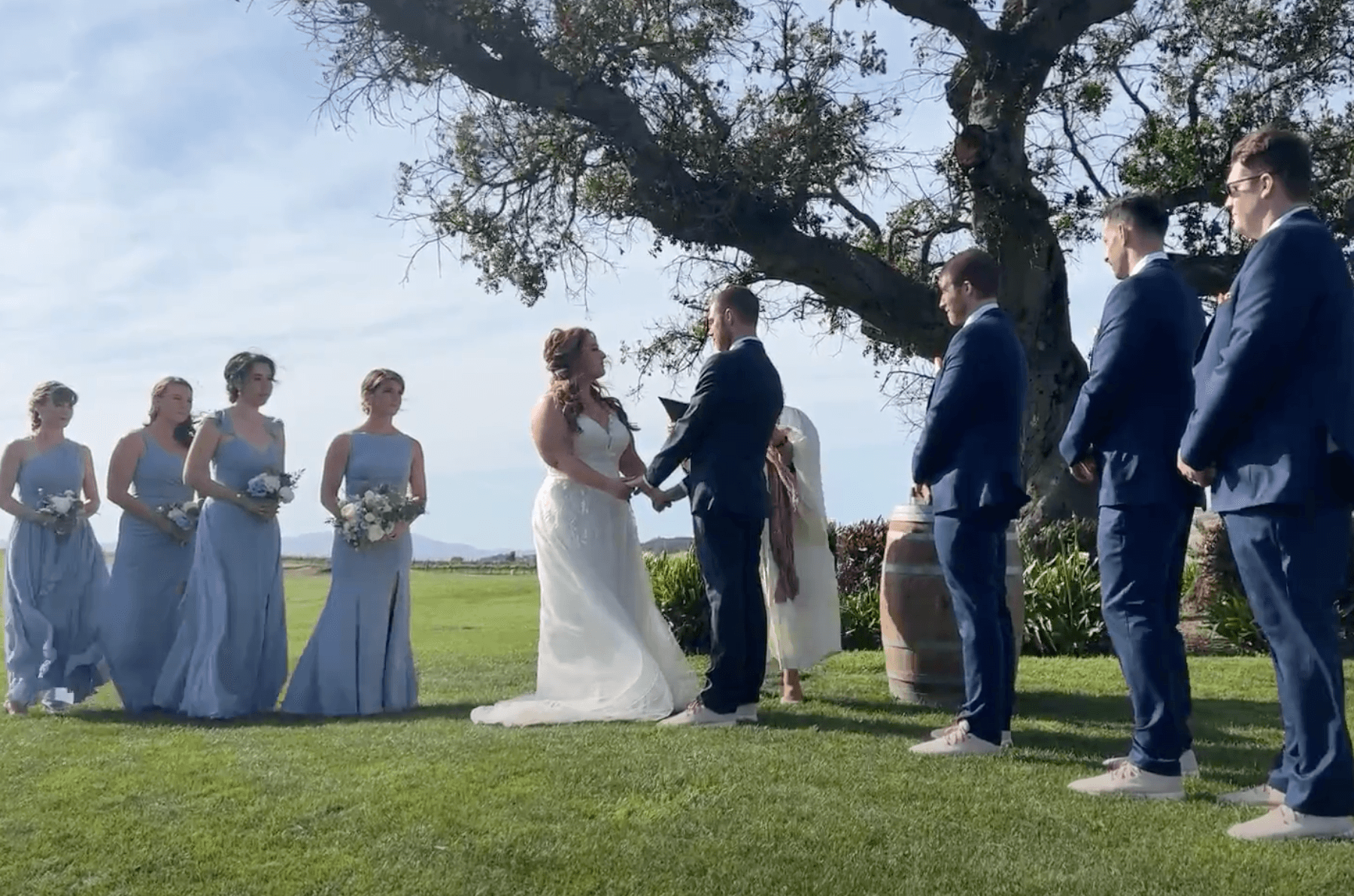 Heather and Glen holding hands during the ceremony, flanked by their wedding party